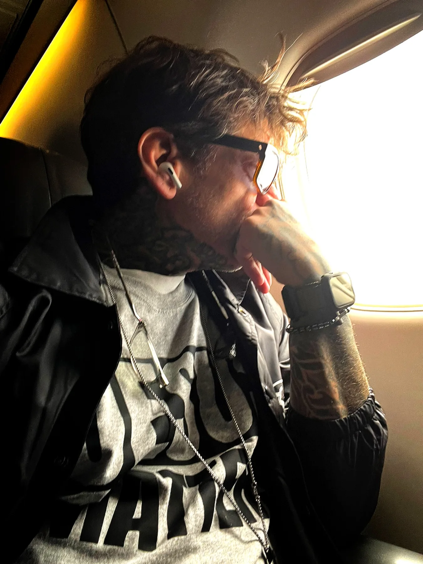 Tattooed man looking thoughtfully out of an airplane window