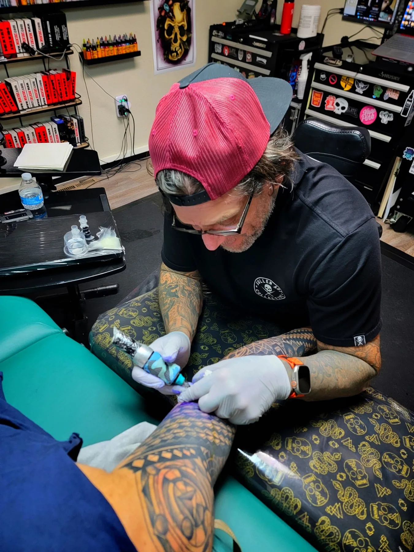 Tattoo artist working with a client in a studio, wearing a red cap